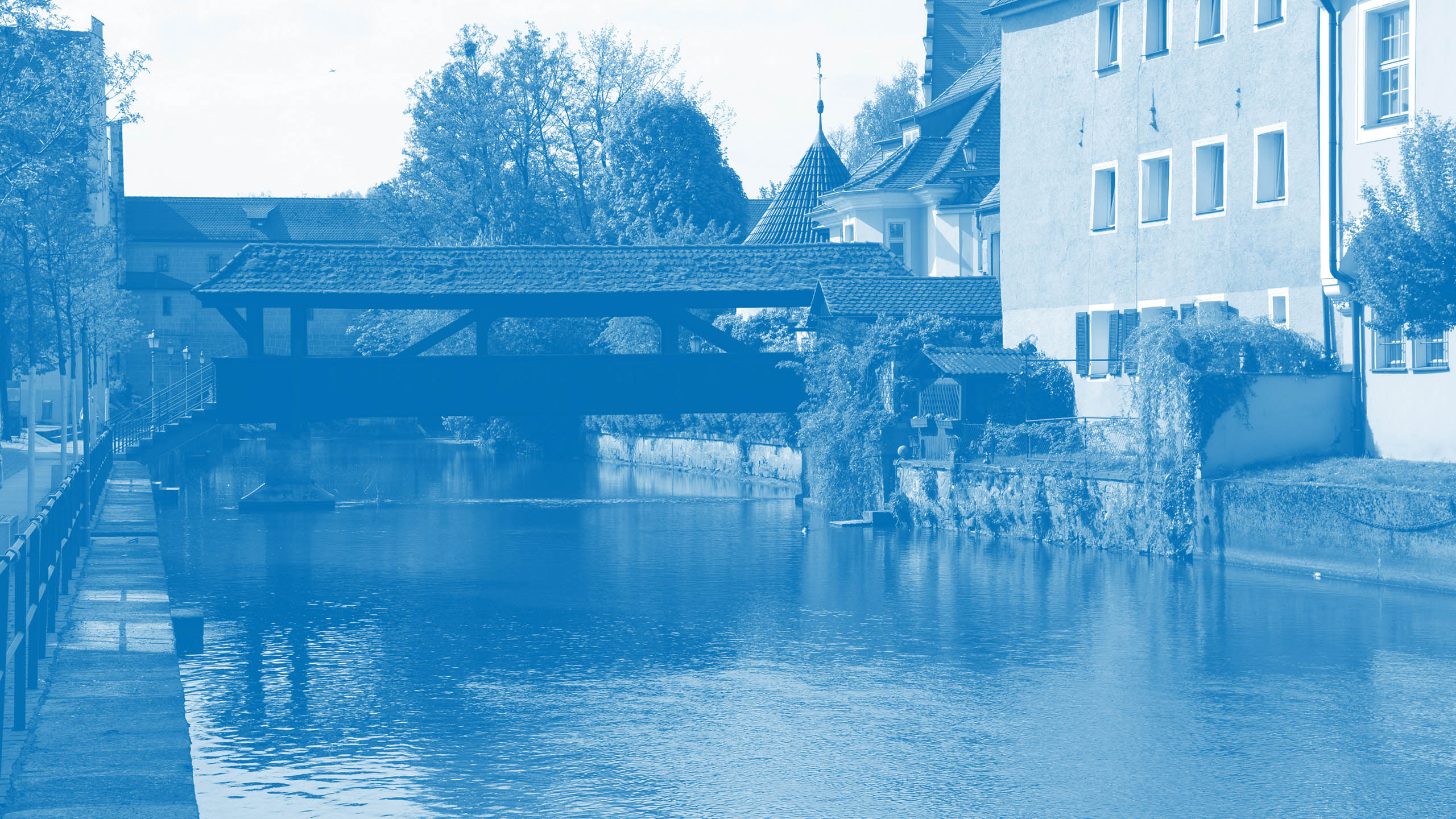 Blick auf einen Fluss mit überdachter Brücke und Häusern am Ufer als Hintergrundbild für den Markenwert „Zuverlässigkeit“ von Oberpfalz Medien.